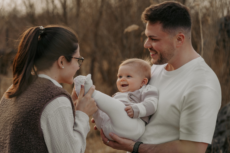 Familienshooting, Kind ist beim Vater auf dem Arm und wird von der Mutter an den Füßen ausgekitzelt