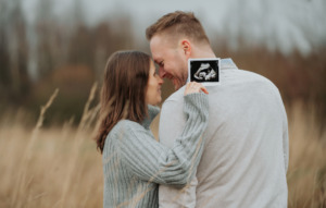 Babynewsfotoshooting, werdende Mutter und Vater schauen sich an und halten ein Ultraschall ins Bild.